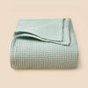 A light mint green waffle textured blanket folded neatly on a neutral background.