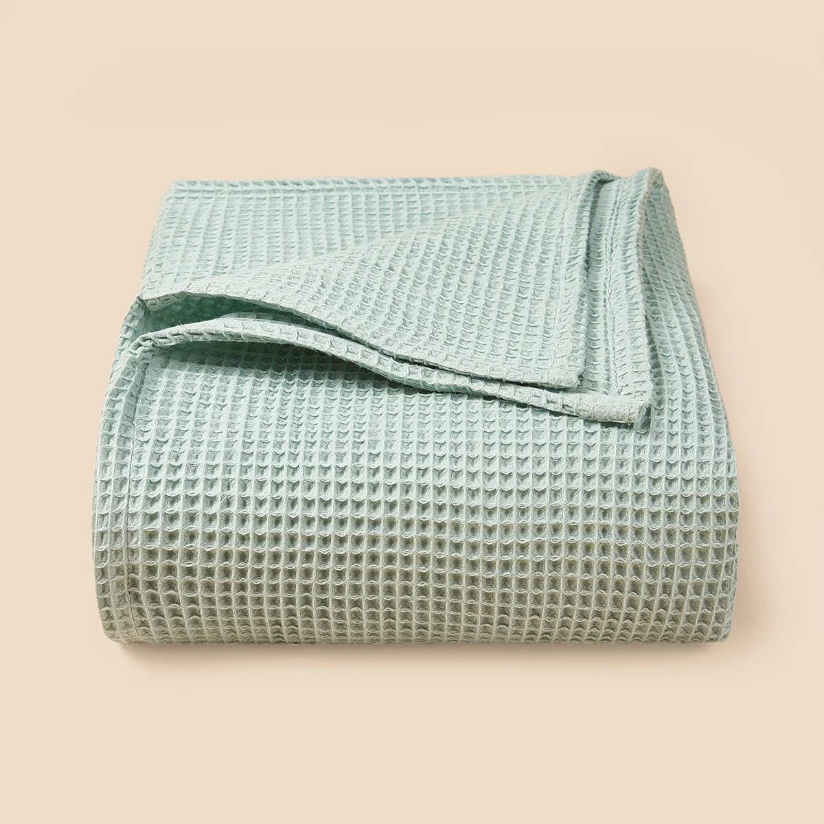 A light mint green waffle textured blanket folded neatly on a neutral background.