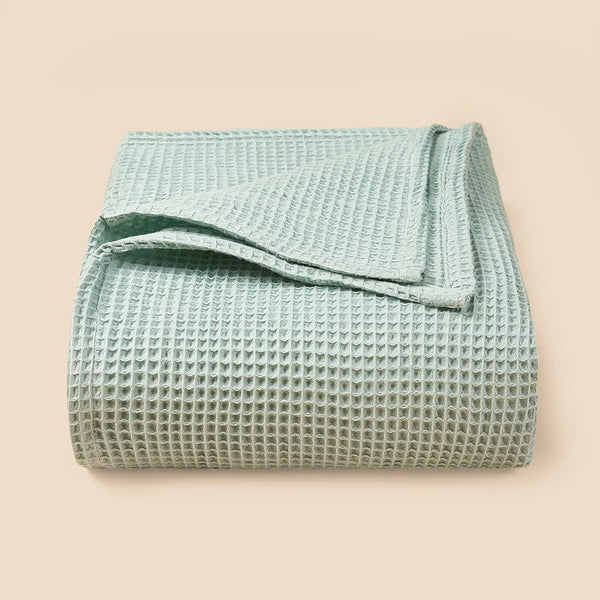 A light mint green waffle textured blanket folded neatly on a neutral background.