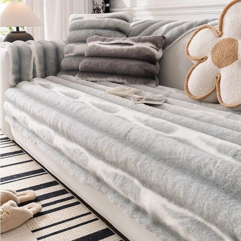Gray plush velvet sofa protector covers stacked on a light gray bed with decorative pillows.
