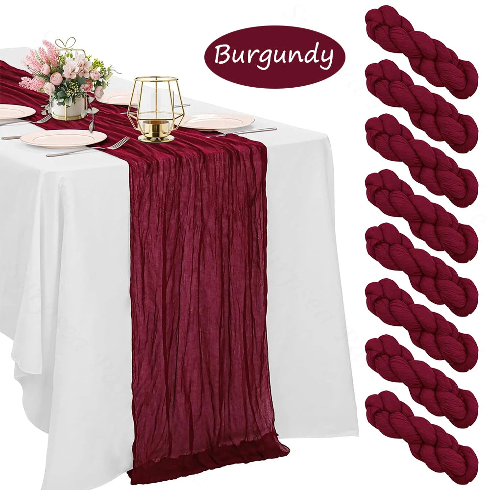 Burgundy cheesecloth table runner draped on a white tablecloth with pink flowers and gold accents.