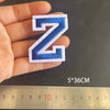 A hand holds a blue alphabet letter N embroidery iron-on patch against a ruler.