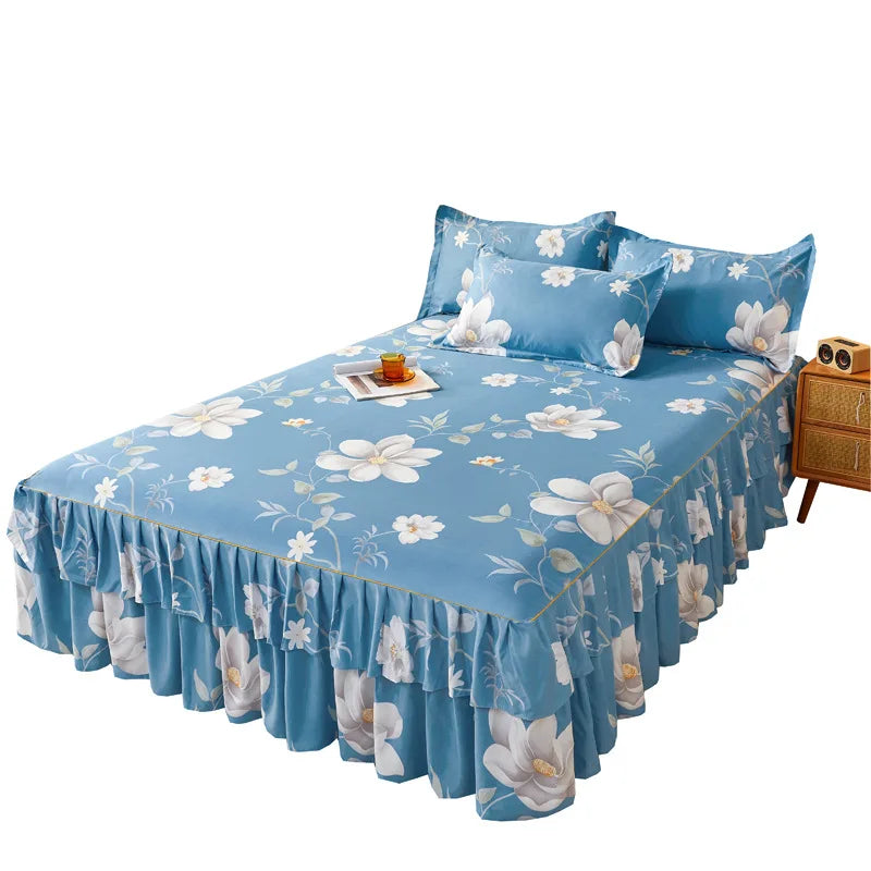 A blue floral printed bed skirt with ruffled layers and white flower accents on a bed.