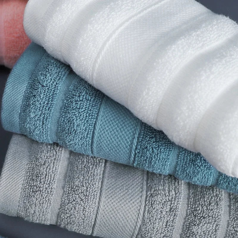A stack of four textured face towels in white, teal, gray, and light gray tones.