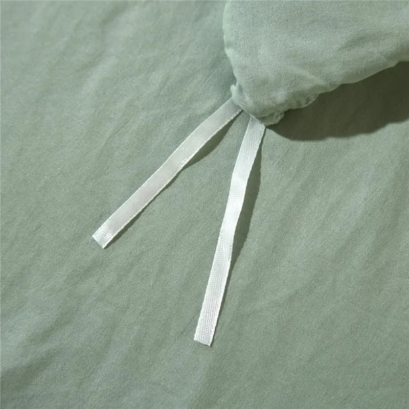 A light sage green duvet cover set with a pom-pom decoration tied at the top.