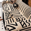 A beige knit sofa protector featuring a black geometric pattern with a small cup on the surface.