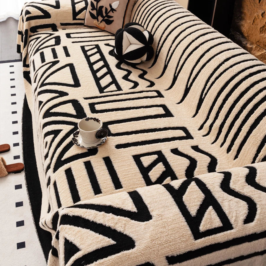 A beige knit sofa protector featuring a black geometric pattern with a small cup on the surface.