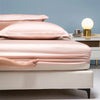A close-up of a pink luxury bamboo bedding set on a bed with a light blue wall and bedside table.