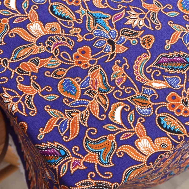 Close-up of deep purple linen fabric with intricate orange and blue floral patterns.