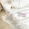 White quilt bedspread featuring delicate floral embroidery and a pink graphic print on a bed.