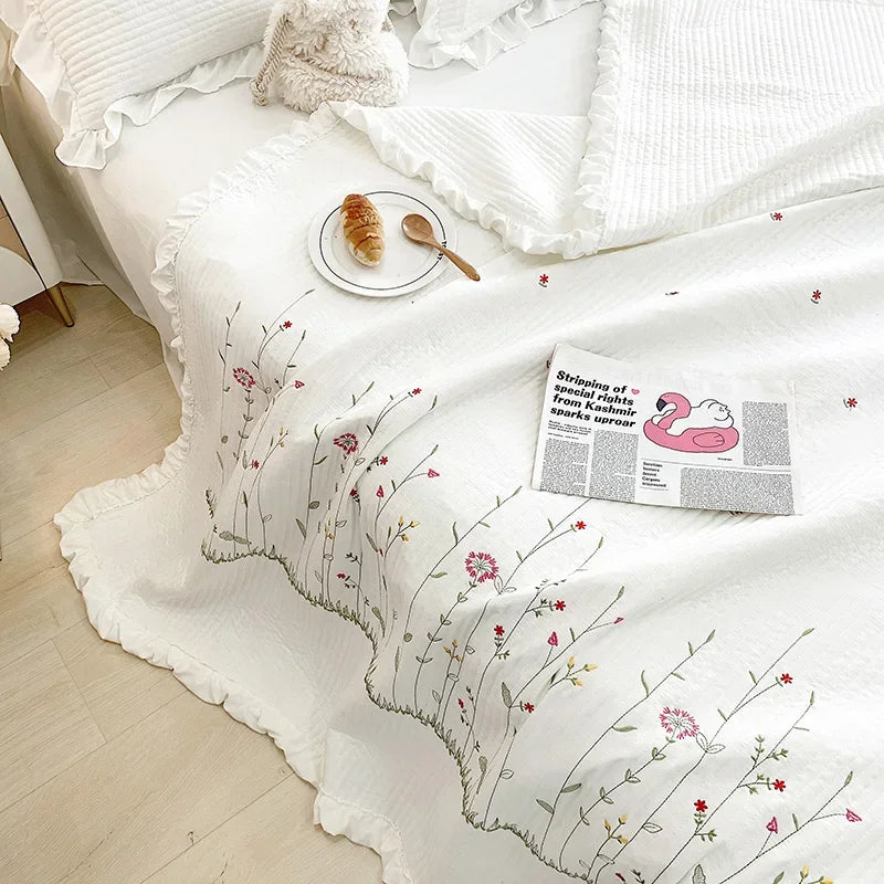 White quilt bedspread featuring delicate floral embroidery and a pink graphic print on a bed.