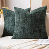 A dark green boucle texture throw pillow resting on a white sofa with a cream knit blanket.
