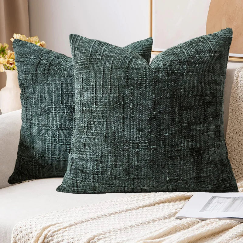 A dark green boucle texture throw pillow resting on a white sofa with a cream knit blanket.