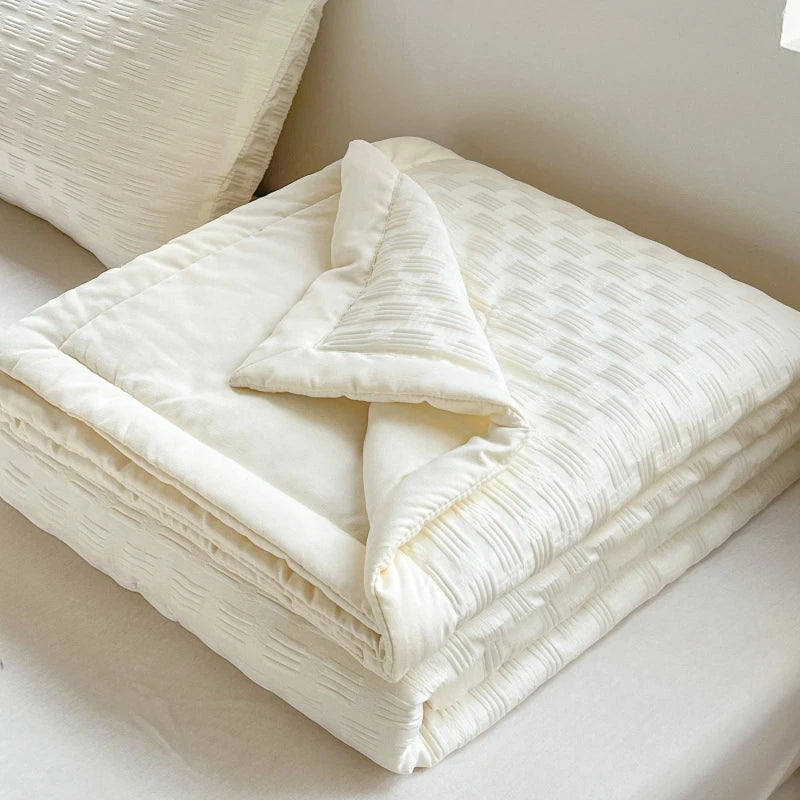 A stack of white breathable waffle quilt blankets folded neatly on a bed.
