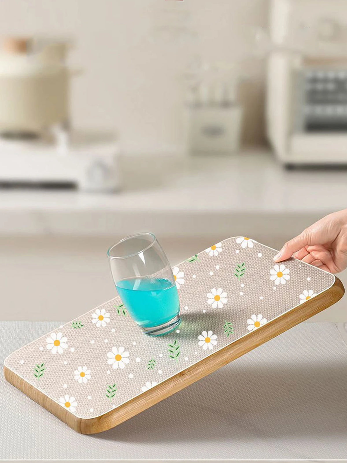 A reusable silicone drawer mat with a floral pattern is placed under a glass of blue liquid on a light surface.