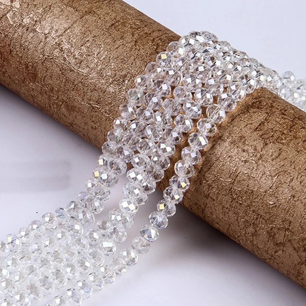 A strand of clear faceted rondelle glass beads is unwrapped and laid across a brown cylindrical object.