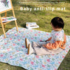 A baby is playing on a waterproof and reusable anti-slip mat outdoors on the grass.