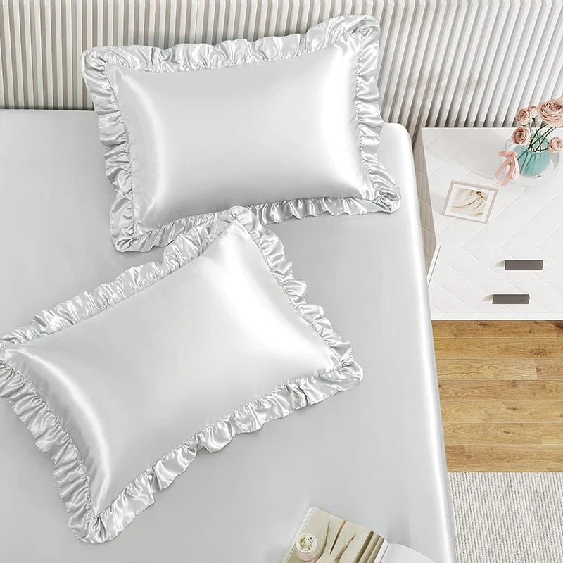 A set of two white ruffled satin pillowcases with silky envelope closures displayed on a white surface.