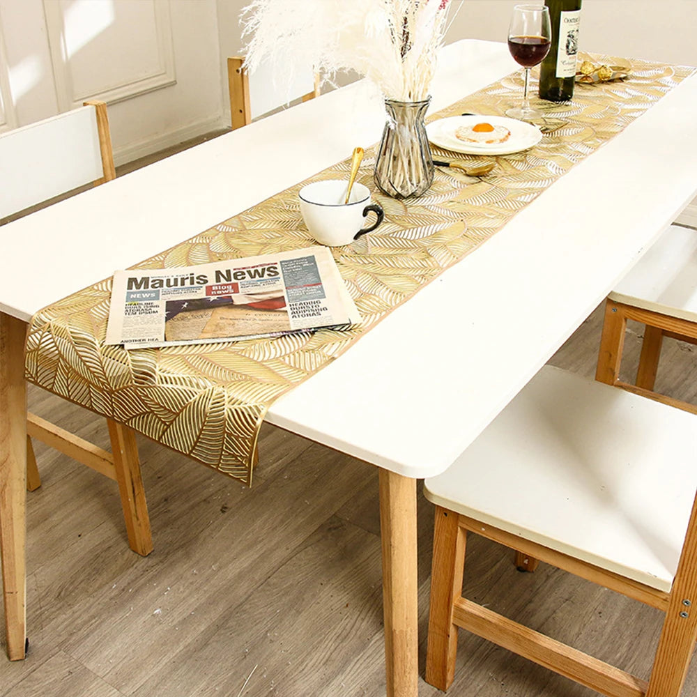 A long white dining table set with a gold patterned runner, wine glass, and floral arrangement.