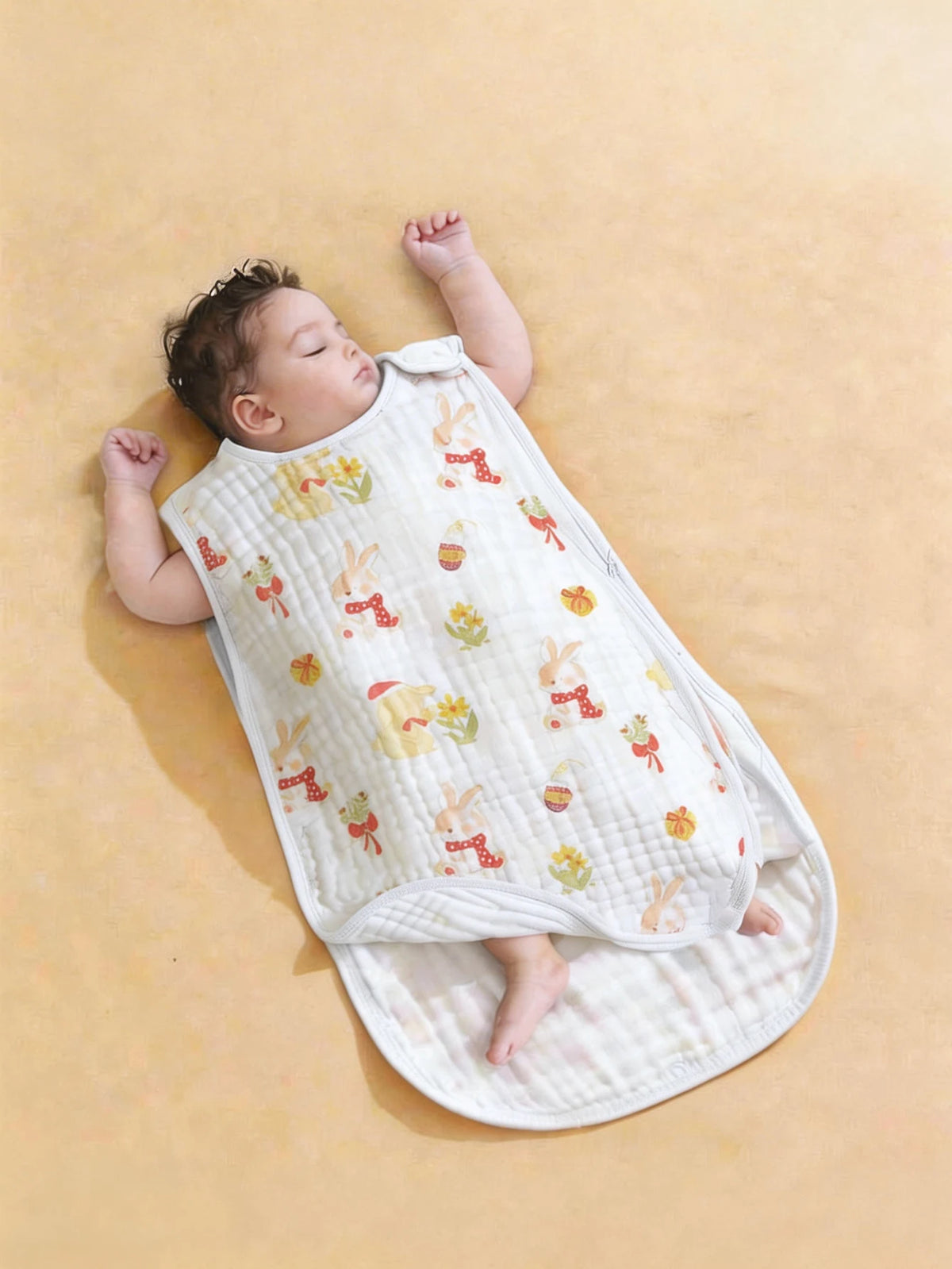 A baby is lying on a white quilted sleeping bag with colorful embroidered patterns on a beige background.