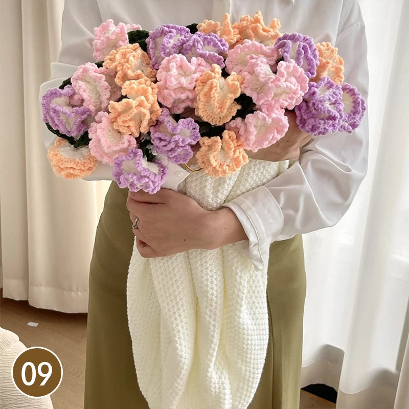 A hand knitted floral rose bouquet arrangement with pink and purple flowers held by a person wearing a white shirt and a crea