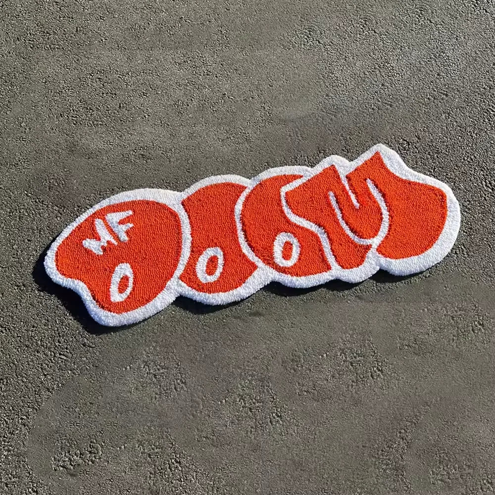 An orange embroidered floor mat featuring the text OOOT and MF
