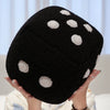 A black dice-patterned plush throw pillow with white spots being held by a person.