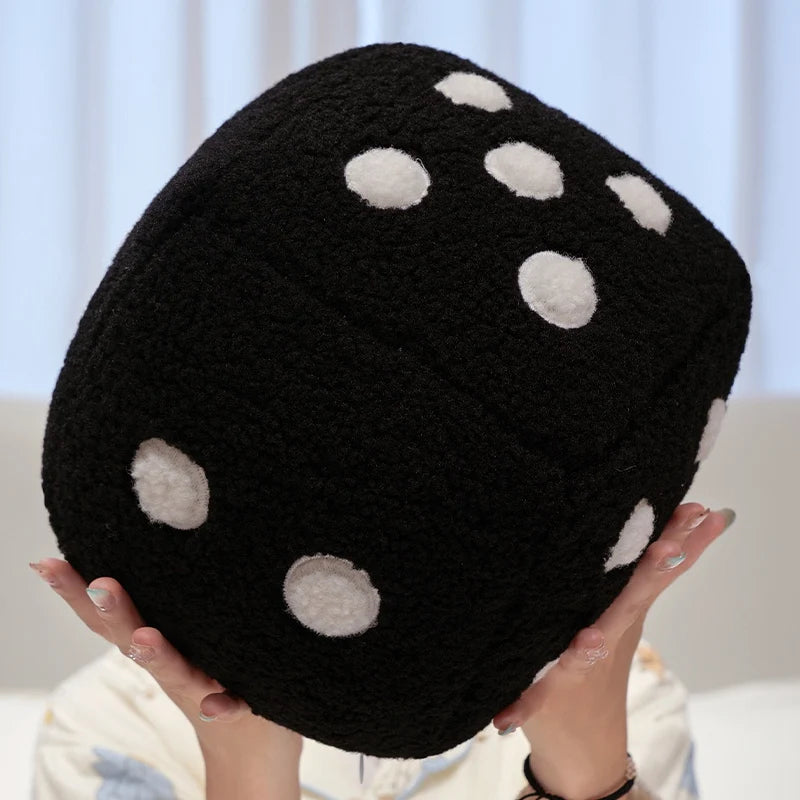 A black dice-patterned plush throw pillow with white spots being held by a person.