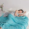 A woman is relaxing under a bright blue quilted blanket in bed, enjoying a beautiful summer night.