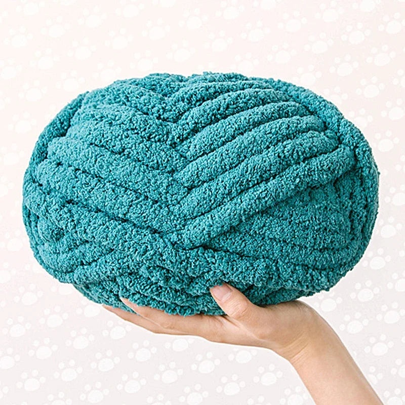 A hand is holding a teal blue hand-knitted wool finger line scarf with a textured, coiled appearance.