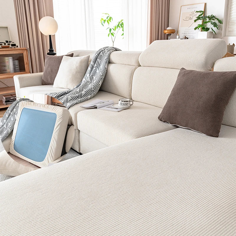 A light beige plush elastic sofa cushion cover with gray and brown accent pillows on a modern sofa.