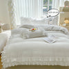 A white ruffled duvet cover set displayed on a bed with sheer white curtains in a bright room.