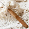 A wooden crochet and knitting needle is resting on a cream-colored knitted fabric.