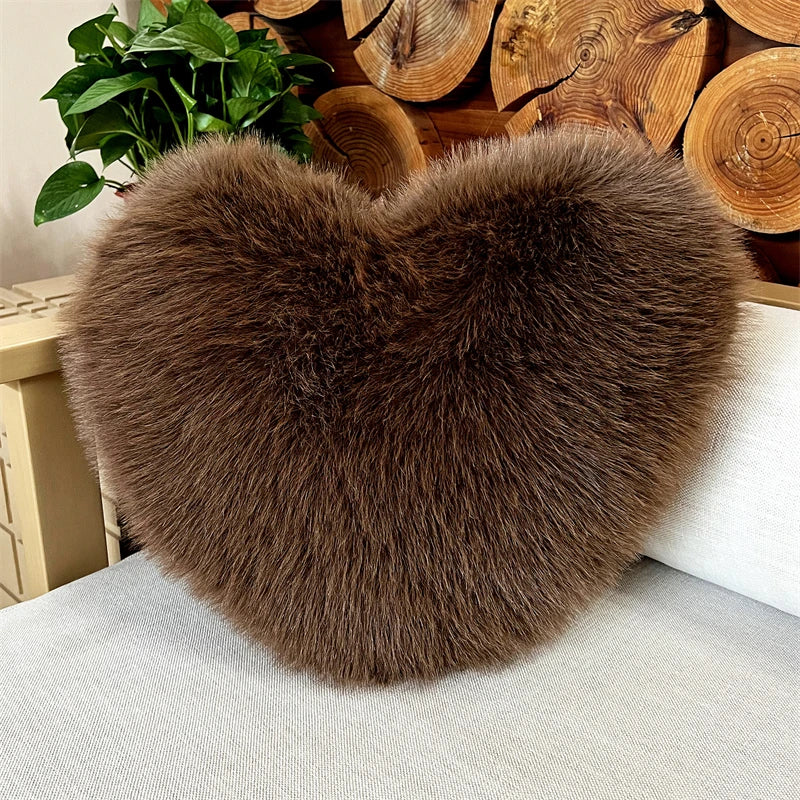 A plush, heart-shaped throw pillow made of brown fox fur resting on a light-colored sofa.