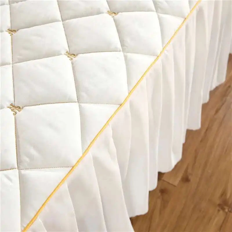 White quilted bed skirt with gold embroidery covering a mattress edge.