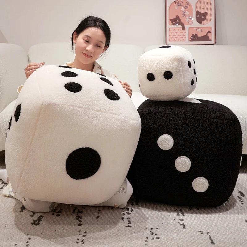 A woman is sitting on a sofa with two oversized black and white dice plush pillows.