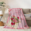 A pink floral knit blanket featuring roses and pink stars draped over a beige sofa.