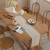 A wooden table is set with a vintage crochet lace table runner and various ceramic items.