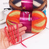 A hand is holding a vibrant gradient dyed wool yarn with orange and pink colors, wrapped in purple fabric.