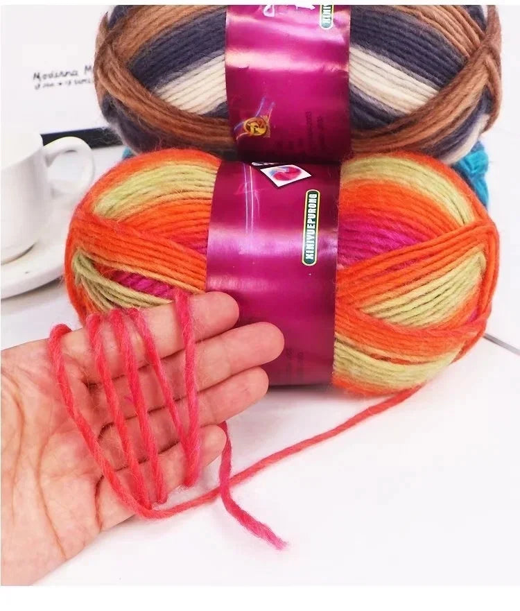 A hand is holding a vibrant gradient dyed wool yarn with orange and pink colors, wrapped in purple fabric.