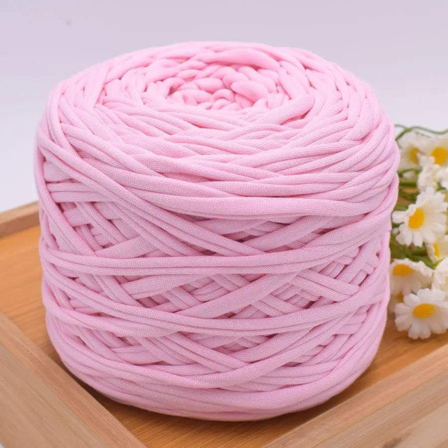 Pink craft yarn in a ball is displayed on a wooden surface.