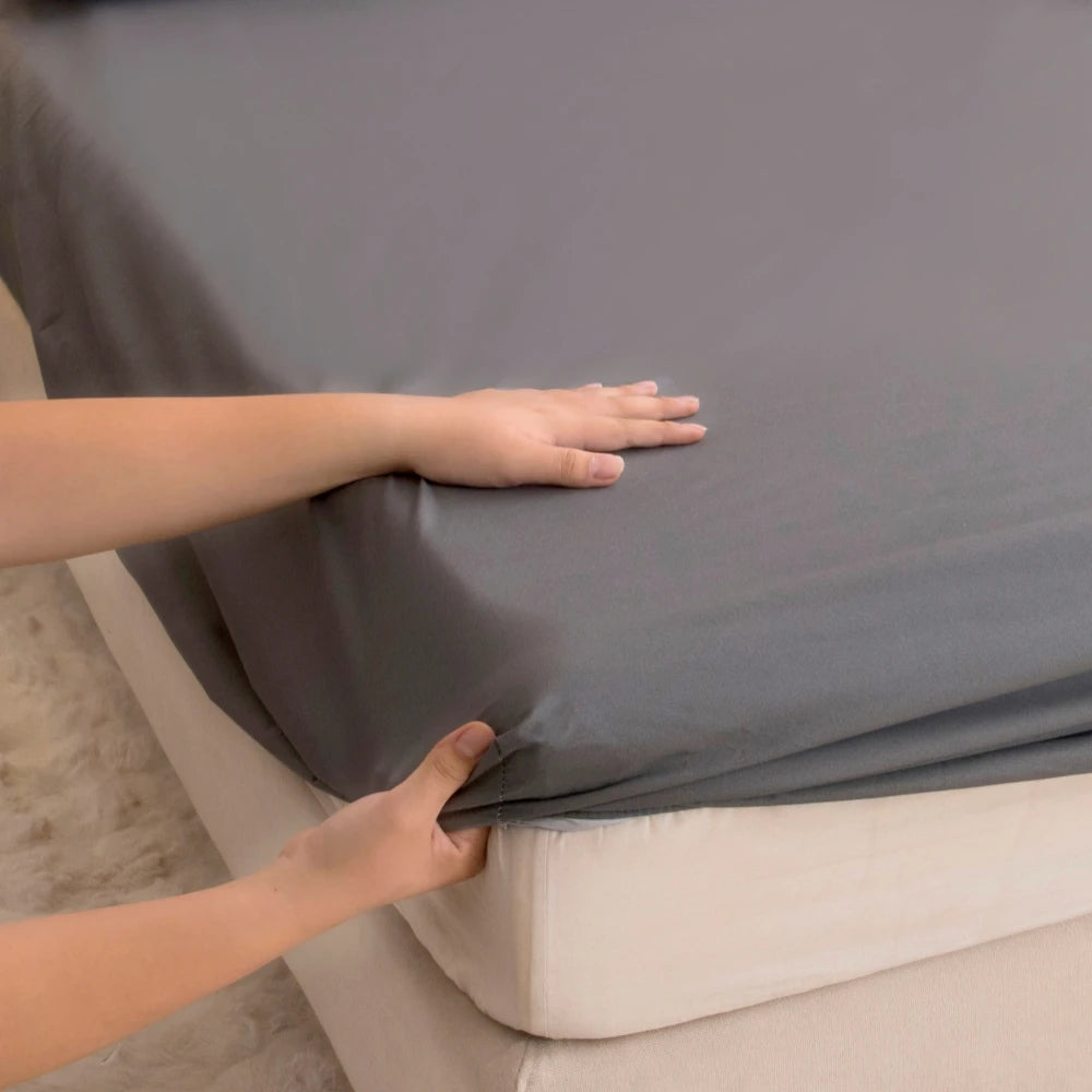 A hand is adjusting a gray waterproof fitted bed sheet on a mattress.
