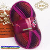 A skein of gradient dyed wool yarn in shades of purple, pink, and red is displayed next to a box.