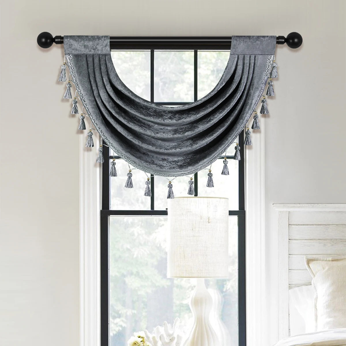 Gray velvet window curtain valance with silver tassels hanging over a window.