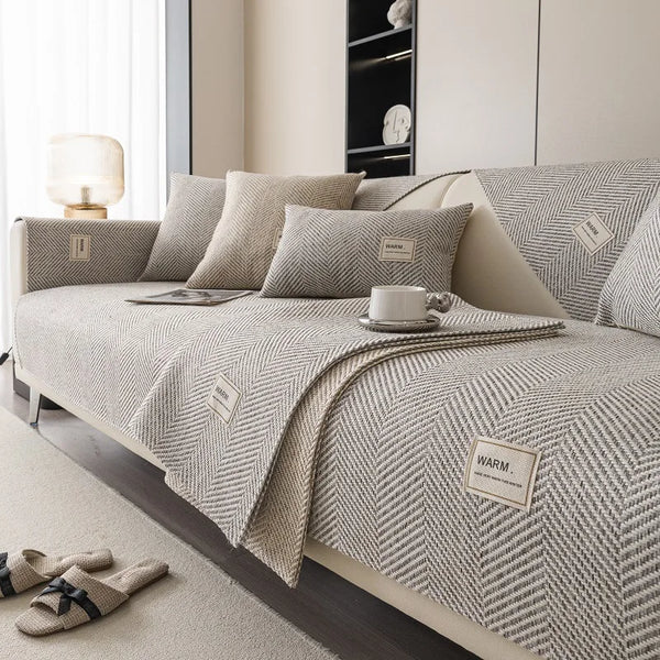 A beige linen sofa cover with textured cushions and a matching throw blanket displayed on a light-colored sofa.