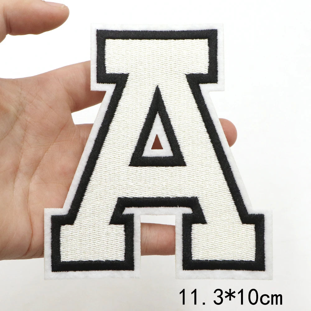 A letter patch shaped like the letter A in black and white embroidery held by a hand.