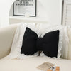 A black bow-shaped sofa cushion with lace trim resting on a white sofa.