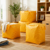 A stack of bright yellow heavy duty foldable storage sacks on a wooden floor next to a window.