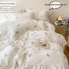 White embroidered rose duvet cover set displayed on a bed with pillowcases and care instructions.