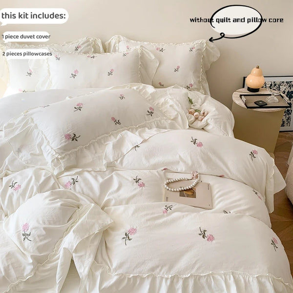 White embroidered rose duvet cover set displayed on a bed with pillowcases and care instructions.